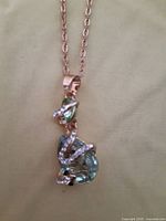 Necklace with a snake design wrapped around a light green faceted prism gemstone pendant, hanging from a chain with rose-gold color.