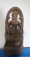 Full view of solid carved teak wood sculpture statue showing figure seated within an arched design.