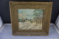 Front view of vintage painting of a cottage in winter landscape, framed in textured wood frame.