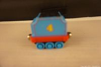 Photo of blue metal box-shaped toy train car from side with blue wheels and red base