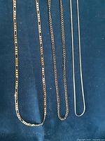 Three chains laid out on blue fabric background showing different styles and thicknesses.