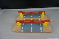 Two wooden railway draw rails with painted road and movable orange barriers on yellow supports placed on grey surface