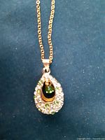 Close up of the teardrop pendant showing clear zircon chips surrounding the oval green stone set in gold-tone metal.