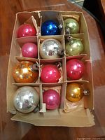 12 mercury glass Christmas balls in original cardboard box with dividers showing varied colors and condition.