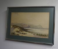 Frontal image showing the entire watercolour painting framed in a modern metal frame with blue mat. The coastal landscape with dunes and a lighthouse is visible.