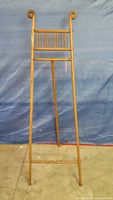 Full frontal image of the antique Victorian wooden easel with scroll top details, tripod stand, and blue backdrop.