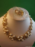 Front view of the bib style faux pearl and rhinestone necklace displayed on a mannequin bust, with matching pierced earrings packaged in plastic placed at the top.