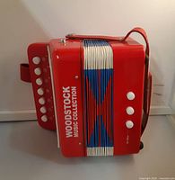 Front view of red Woodstock Music Collection toy accordion showing white buttons and colorful bellows