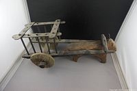 Front view of the primitive folk art wooden ox and cart showing the ox's head, wooden body, and two wooden disc wheels attached to the cart frame.