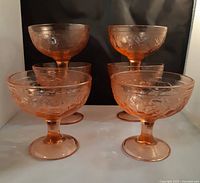 Six pink pedestal compote bowls arranged with two elevated on the back and four in the front, showing overall shape and color.
