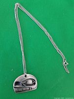 Full view of the silver-tone metal chain and attached carved metal pendant against green background.