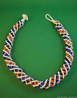 Full view of the 18 1/4 inch long indigenous tubular beaded necklace laid on a green background, showing its loop closure and spiral design.