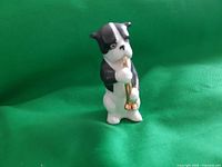 Front angle photo of the miniature ceramic dog figurine playing a golden wind instrument on a green background.