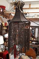 Front view of the dark chocolate brown handmade macrame chandelier with fringed skirt hanging in interior space.