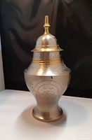 Full view of urn with lid on, showing overall shape, size, and etched silver overlay designs on brass.