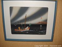 Full view of the framed art depicting a boat and lighthouse scene on layered stoneware with a blue frame and white matting.