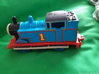 Side angle of the blue Thomas the Tank Engine toy train showing number 1 and red base with visible wear on black tender section.