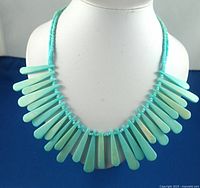Full view of turquoise bib necklace on white display bust showing all spiked beads in a semicircle formation