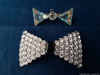Photo showing both rhinestone bow pins, larger Thelma Deutsch signed pin at bottom, smaller faceted clear crystal bow at top on dark background.