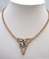 Front view of vintage rhinestone necklace on a display bust showing gold-tone chain with clear rhinestones and triangle pendant with large iridescent rhinestones.
