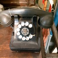 Front top-down view of the black bakelite rotary phone showing dial and handset resting on cradle. Surface wear and some scuffing visible.
