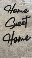 Photo showing the three separate black MDF wood words 'Home', 'Sweet', and 'Home' arranged on a fabric surface.