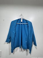Blue August Silk cardigan hanging on white hanger displayed on wall.