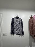 Full view of the cardigan hanging on a hanger against a white wall, showing the open front and the blue and white diamond knit pattern.