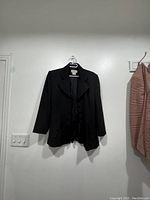 Front view of the black blazer hanging on wall.