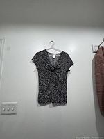 Front view of the black and white spotted blouse hanging on a hanger against a wall.