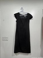 Front view of a black fitted dress hanging on a hanger against a light background.