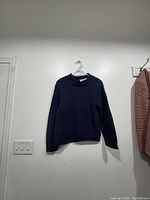 Navy blue knitted sweater hung on white hanger against a wall.