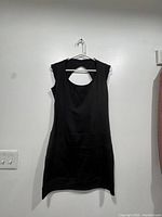 Full front view of black sleeveless Guess dress on white hanger against wall.