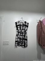 Full view of the black and white patterned dress hanging on a white hanger against a wall.