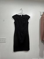 Front view of a black fitted dress with cap sleeves on a hanger against a white wall.