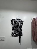 Front view of Mandy Evans blouse hanging on wall, showing black and white stripes and waist tie detail.