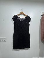 Full front view of a black lace women's dress on a wooden hanger against a white wall.