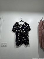 Full front view of black blouse with white and pink floral print hung on wall.