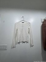 Full view of white long sleeve top hanging on a white plastic hanger showing front and sleeve length.