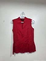 Full front view of the red sleeveless top hanging on a white hanger against a plain white wall, showing the cut and color of the garment.