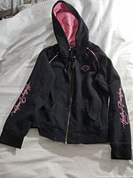Full view of black Harley Davidson women's hoodie with pink accents, laid flat showing front zipper and hood.