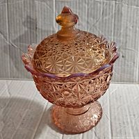 Side angled view of pink L.E. Smith Daisy & Button candy dish with lid showing detailed pattern and scalloped edge.