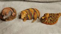 Three animal figurines arranged on fabric background: a beaver on a base, a multicolored sheep, and a duck with floral pattern.