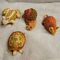 Four figurines displayed on a soft surface including frog, snail, mouse, and turtle.