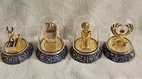 Front view of all four Franklin Mint Egyptian statue figurines under glass domes on blue decorated bases with hieroglyphs.