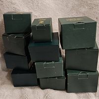 Stack of 12 green boxes housing Harmony Kingdom figurines, some stacked and some tilting, on a cloth background.