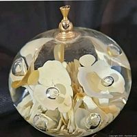 Top view of round clear glass paperweight showing white and cream flower design inside glass and brass fixture on top