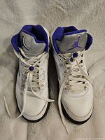 Overhead photo of pair of Nike Air Jordan 5 Retro Concord sneakers showing white upper with purple Jumpman logo on silver tongue, purple lining, and white laces with lace locks.
