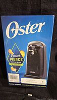 Photo of the blue retail box showing Oster electric can opener image and branding, stating Power Pierce cutting blade feature