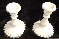 Pair of white Fenton Silver Crest milk glass candlesticks with ruffled silver-edged bases on black background showing front and side angles.